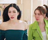 two women standing next to each other with one wearing a green jacket and the other wearing a blue off the shoulder top