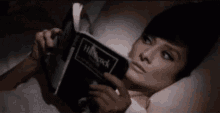 a person is holding a book in their hands while laying in bed .