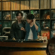 two men are standing next to each other in front of a shelf with records on it .