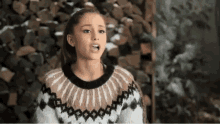 a woman wearing a sweater is standing in front of a pile of logs and making a funny face .