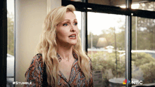 a woman is standing in front of a window with the nbc logo on the bottom