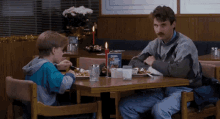 a man and a boy are sitting at a table in a restaurant with a sign on the table that says ' school lunch '