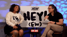 a man and a woman are sitting in front of a sign that says hey