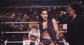a woman in a wrestling ring holds up a championship belt