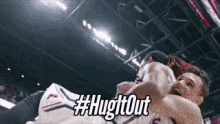 two basketball players are hugging each other in a stadium and the words hug it out are visible .
