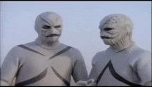 two men wearing white masks and gloves are standing next to each other .