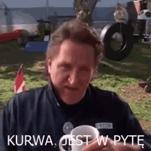 a man in a blue jacket is holding a white cup with the words kurwa jest w pyte on it