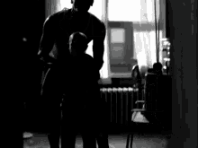 a black and white photo of a man standing in front of a window in a room .