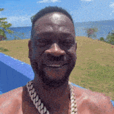 a shirtless man wearing a chain around his neck smiles