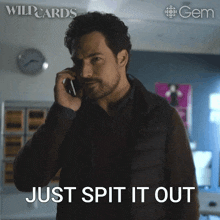 a man talking on a cell phone with the words just spit it out behind him