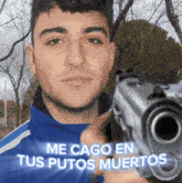 a man in a blue jacket is pointing a gun at the camera with the words me cago en tus putos muertos on the bottom