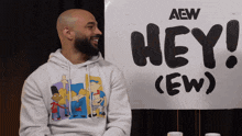 a man in a white hoodie stands in front of a sign that says hey