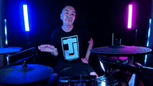 a man in a black shirt with the letter t on it is playing drums