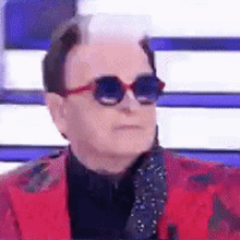 a man wearing sunglasses and a red jacket looks at the camera .