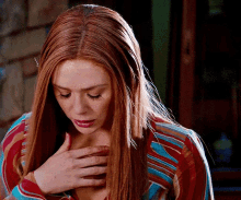 a woman with long red hair is holding her chest .