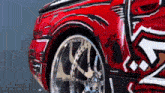 a red car with chrome wheels and a graffiti design on it