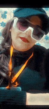 a woman wearing sunglasses and a hat is holding a cell phone .