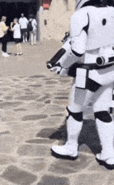 a storm trooper is walking down a stone sidewalk with a gun .