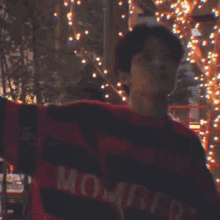 a man in a red shirt stands in front of a christmas tree