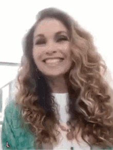 a woman with long curly hair is smiling and wearing a white shirt and a green jacket .