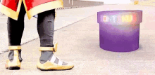 a person in a superhero costume is standing next to a purple container on the ground .