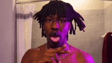 a shirtless man with dreadlocks looks at himself in a mirror