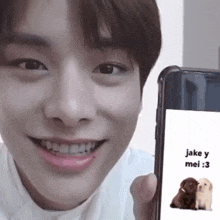 a young man is smiling while holding a cell phone with a picture of two dogs on the screen ..