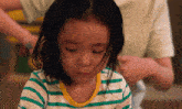 a little girl wearing a green and white striped shirt looks down