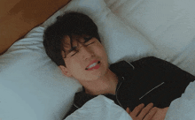 a man in a black shirt is laying on a bed with a white pillow .