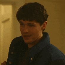 a young man wearing a blue jacket is smiling and looking down