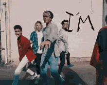 a group of young men are dancing in front of a brick wall with the word i 'm written on it .