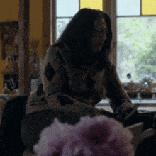 a woman in a plaid sweater sits in front of a window reading a book