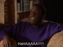 a man in a purple sweater is laying on a couch and laughing