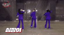 three women in purple suits are dancing in front of a wall that says the bomb dance on it