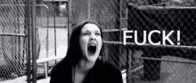 a woman is screaming in front of a chain link fence and the word fuck is written on the fence .