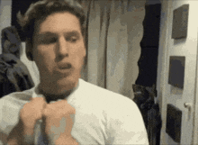 a man in a white shirt adjusts his tie in front of a mirror