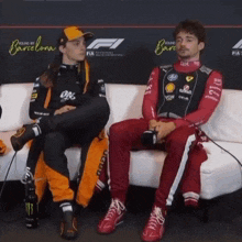 two race car drivers sit on a white couch in front of a sign that says barcelona