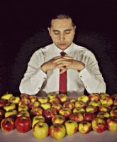 a man in a white shirt and red tie is sitting at a table full of apples