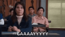 a group of people are sitting in a classroom with a woman sitting at a desk .