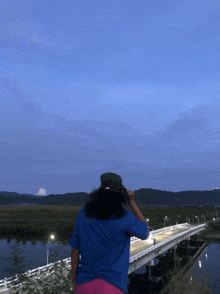 a woman in a blue shirt stands on a bridge over a body of water