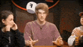 a man in a purple shirt is sitting at a table with two other people and a white cube with the letter f on it .