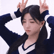 a girl in a blue sweater and pigtails is making a peace sign with her hands on her head .