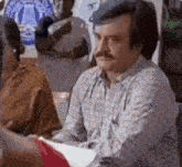 a man with a mustache is sitting at a table in a room .