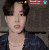 a man in a blue plaid shirt is looking at the camera with a street live advertisement behind him