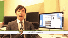 a man in a suit and tie is standing in front of a computer monitor with a green screen behind him