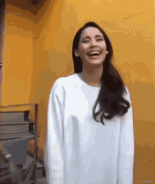 a woman wearing a white sweater is laughing in front of a yellow wall