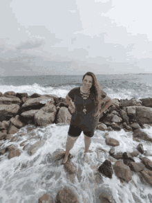 a woman stands on a rocky beach with her feet in the water