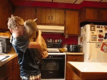 a boy is holding a cat in his arms in a kitchen with a refrigerator and stove