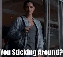a woman is standing in front of a door with the words " you sticking around " on the bottom
