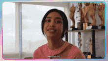 a woman in a pink shirt is smiling in a room with trophies on a shelf .